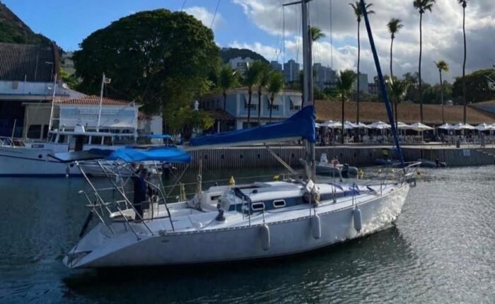 Veleiro Fast 395 atracado em marina, com mastro alto, capa azul da vela e palmeiras ao fundo