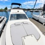 Solário com colchonetes cinza na proa da lancha, com o flybridge e o toldo azul ao fundo na marina